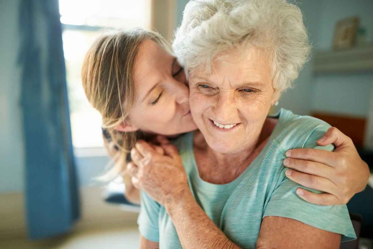 Close-up shot of a caring adult daughter kissing her senior mother at nursing home
